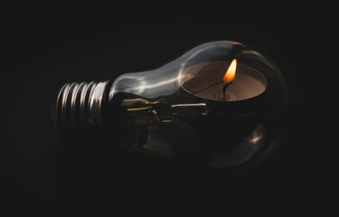Electric lamp and candle on a dark background. Symbol of return to the past. Incandescent bulb and...