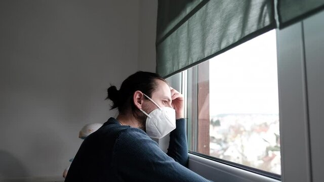 Mann in Quarant&auml;ne wegen Covid-19 mit Mundschutz. Schaut aus seinem Fenster