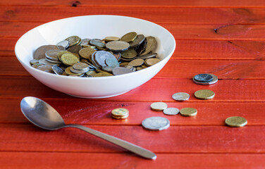 lots of coins in a bowl on red background next to spoon