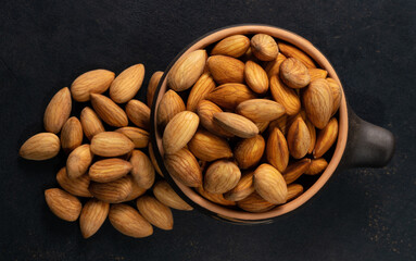 Almonds in a ceramic bowl on a black background, top view