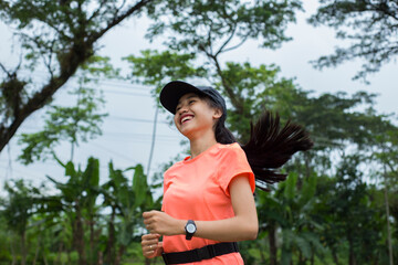 A portrait of a young asian woman doing excercise outdoor in a park, jogging
