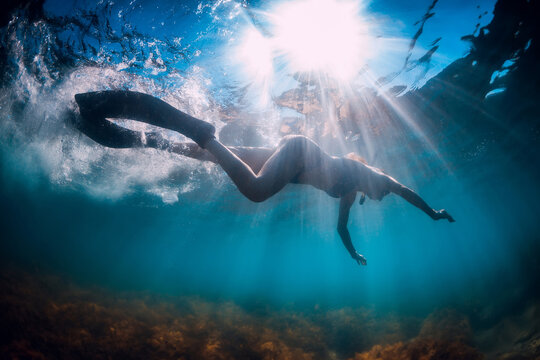 Young woman with fins and mask swim in blue sea with sun rays. Snorkeling underwater in summer ocean
