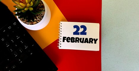February 22 on a multicolored background on a white notebook.Next to it is an artificial flower in a pot .Calendar for February.