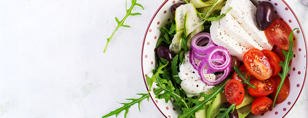 Fototapeta na wymiar Healthy Greek salad of fresh cucumber, tomato, avocado, arugula, red onion, feta cheese and olives. Healthy food, vegetarian dieting. Top view, overhead, banner