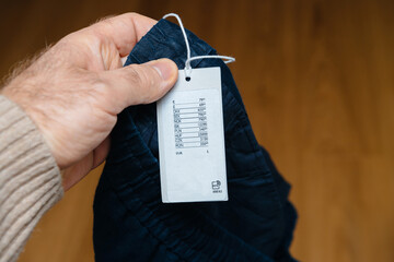 POV male hand holding new pair of pants with price tag in multiple international currencies and...