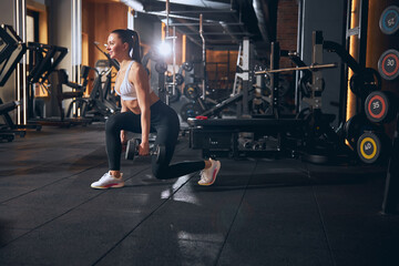Fototapeta na wymiar Joyful young woman doing lunges with weights