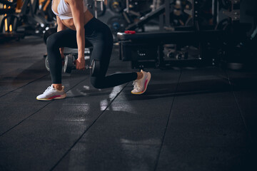 Fit woman exercising legs with dumbbells indoors