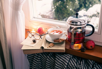Winter relax at cozy home. Hot tea, teapot and book by the window.