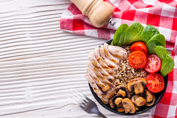bowl of healthy quinoa with grilled chicken and vegetables on a white rustic wooden background