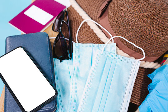 Pandemic travel concept. Passport, medical masks and protective gloves with sunglasses, a hat and a mock up telephone on a blue background. Enlarged photo.