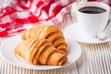 delicious fresh croissant and cup of coffee on a white wooden rustic background