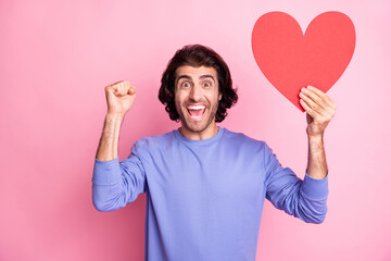 Portrait of impressed guy fist up open mouth hold heart paper card isolated on pink color background