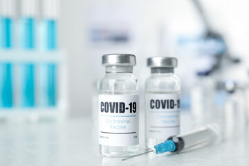 Vials with vaccine against Covid-19 and syringe on white table indoors