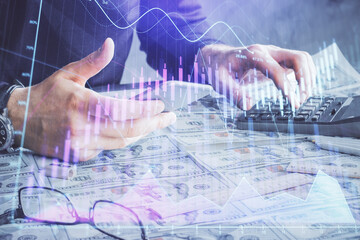 Double exposure of man's hands holding and using a digital device and forex graph drawing. Financial market concept.