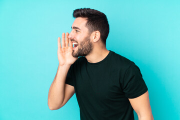 Caucasian handsome man isolated on blue background shouting with mouth wide open to the lateral