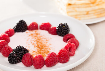 breakfast of raspberries and blackberries with yogurt and pancakes on table