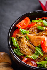 delicious glass noodles with chicken and vegetables on a dark stone background