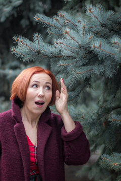 An elderly woman with red hair is surprised. A woman stands next to a blue spruce