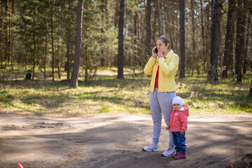 young woman with a baby toddler talking on a mobile phone emotionally in a forest outside the city