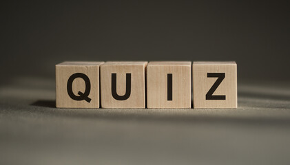A wooden blocks with the word QUIZ written on it on a gray background.