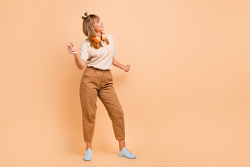 Fototapeta premium Full length photo of cute girl enjoy dancing close eyes wear earphones t-shirt isolated beige color background