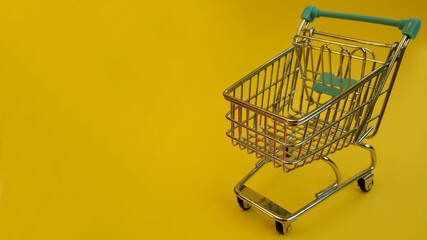 close up a small metal shopping cart with a supermarket on a yellow background side view . sales