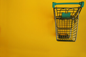 close up a small metal cart with a supermarket on a yellow background top view . sales