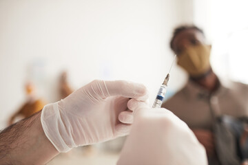 Close up of unrecognizable male doctor holding syringe while vaccinating patients in medical clinic, copy space