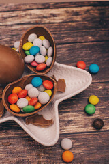 sweet colored chocolate little candies on a white plate, colored sweet pebbles scattered on the wooden background. Chocolate eggs for Easter