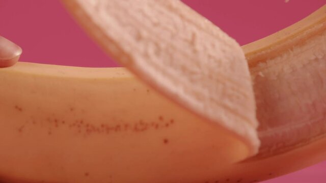 Peeling the banana, close up shot on a pink background