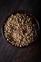Dried coriander seeds in bowl on the dark wooden background
