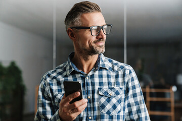 Happy white-haired man in eyeglasses smiling while using mobile phone