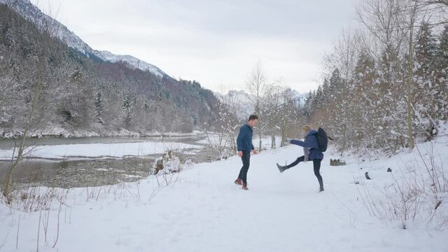 Laughing couple playfully run in a snowy landscape and throw snow at each other. Slow motion wide shot.