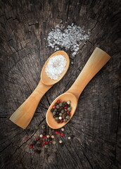 Wooden  spoons filled with salt crystals and black peppercorns. On old wooden background. Vintage effect. 