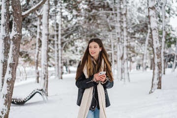 Happy girl in earphones using cellphone while walking in winter forest