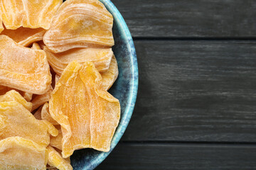 Delicious dried jackfruit slices in bowl on black wooden table, top view. Space for text