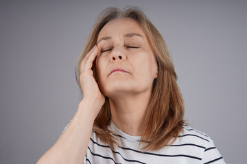 Fototapeta premium senior woman in a striped shirt is holding her head, suffering from pain. Isolate on gray background