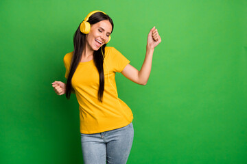 Photo of funky charming young woman raise fist wear headphones music lover isolated on green color background