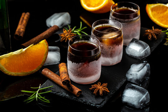 frozen herb liqueur in small glass. Shot glass of herb liqueur with cinnamon and oranges on a dark background