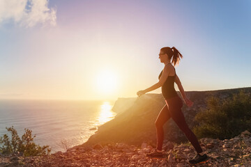 Fit woman walking on the mountain near the sea at sunrise . Healthy lifestyle concept