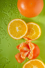 Vertical image of fresh and juicy fruits on the wet green surface.Natural and ripe oranges, tangerine, whole grapefruit