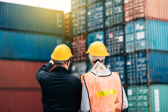workers teamwork man and woman in safety jumpsuit workwear with yellow hardhat and use laptop check container at cargo shipping warehouse. transportation import,export logistic industrial service