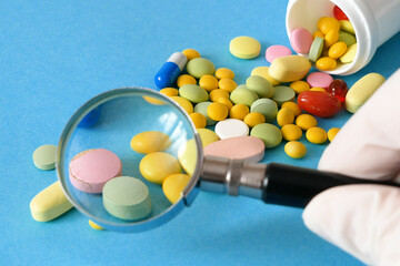 magnifying glass, pills and tablets on blue background. checking ingredients and effectiveness of...