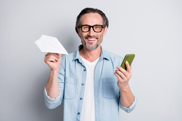Photo of handsome man happy smile hold paper plane origami use cellphone isolated over grey color...