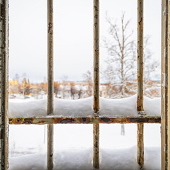 Winter view through a broken prison window with snow covered rusty metal bars