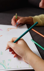 Woman and girl drawing together a coloring with multi-colored pencils, close-up on hand. Home art hobby.