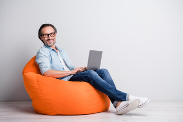 Full length photo of cheerful aged man happy smile sit chair programmer chat type laptop isolated over grey color background - obrazy, fototapety, plakaty