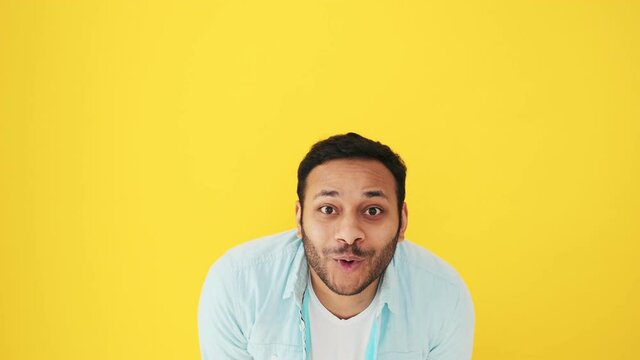 A surprised indian man is looking to the camera while opening his mouth standing isolated over yellow background in studio