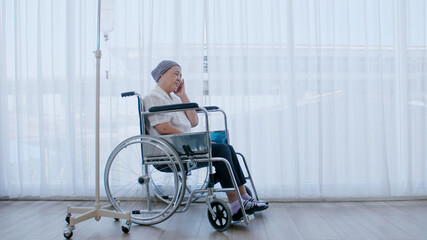 An elderly woman with cancer sits in a wheelchair and she has a headache while being hospitalized.