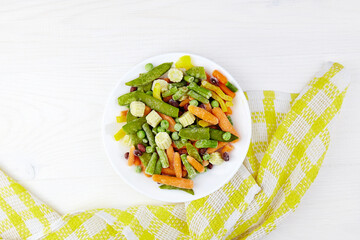Frozen vegetables on white plate:  corn, string beans, pepper, green peas, beans and carrot. Top view with copy space.